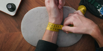 a man measuring his wrist size using a tailor’s tape
